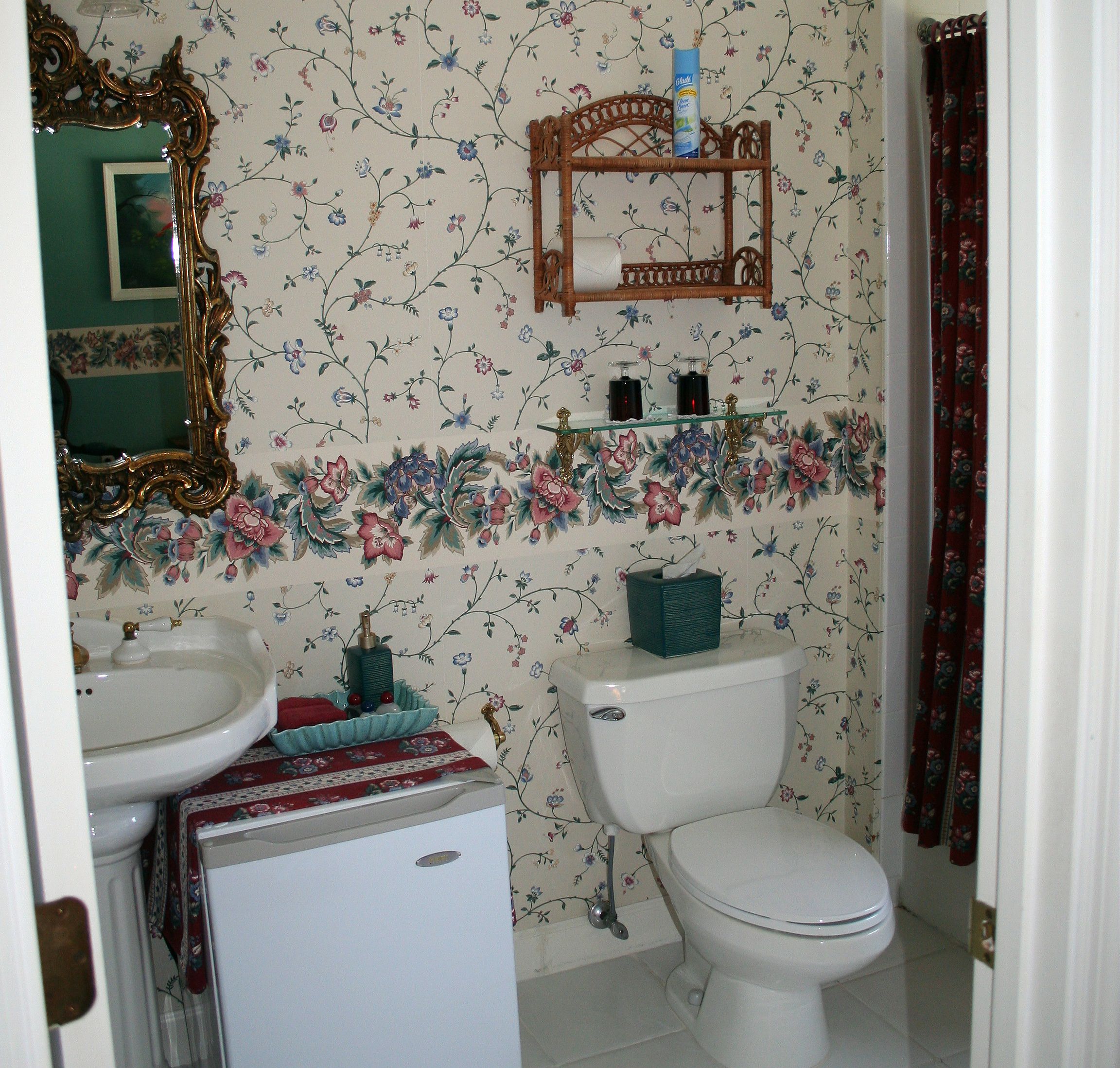 A bathroom with a floral wallpaper, a white sink, a toilet, and a mirror with an ornate frame.