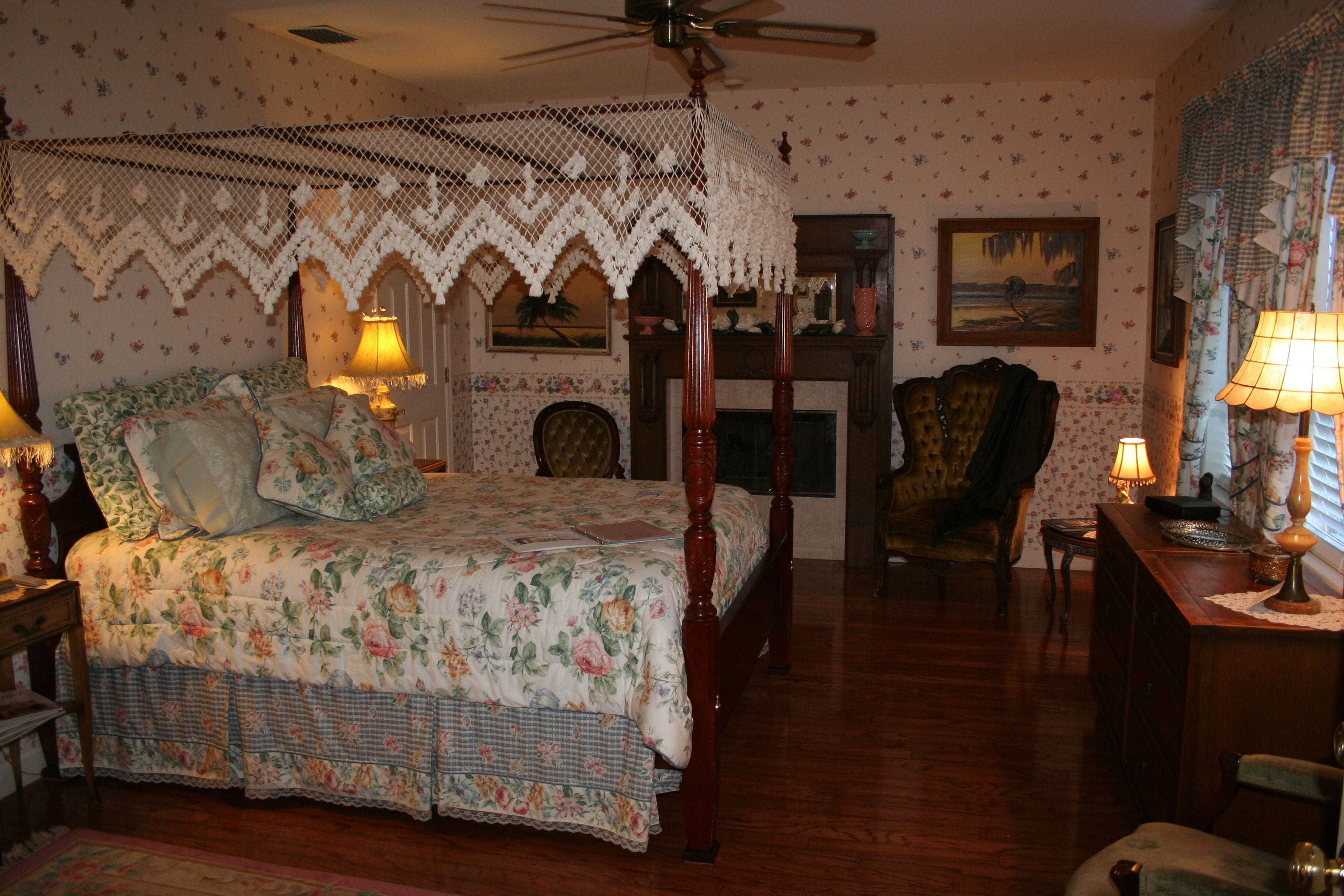Ein Schlafzimmer mit Himmelbett, Holzboden, Kamin und Deckenventilator.