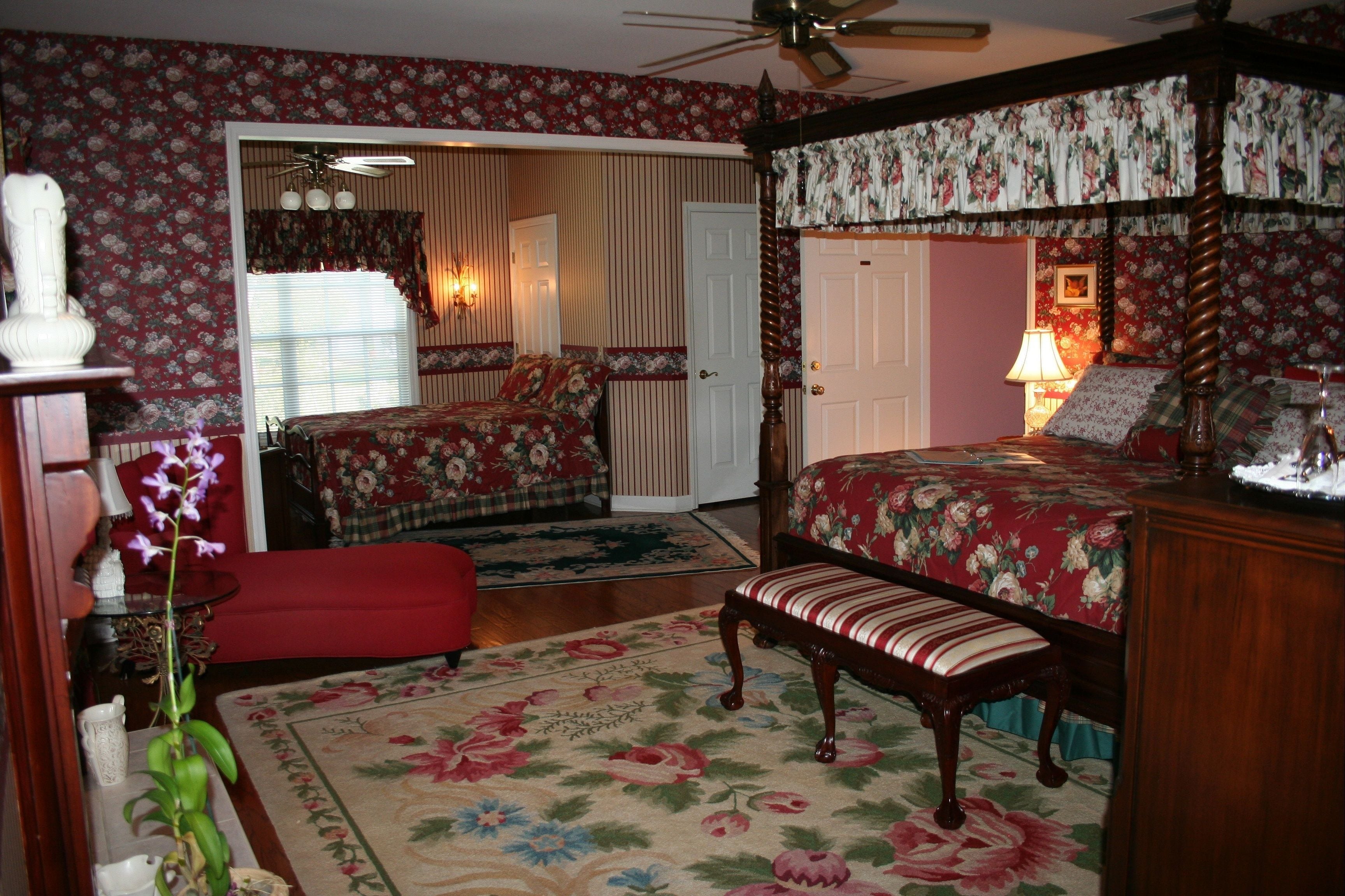 Ein Schlafzimmer mit einem Himmelbett, einer Bank, einem roten Sessel und einem Teppich mit floralem Muster.