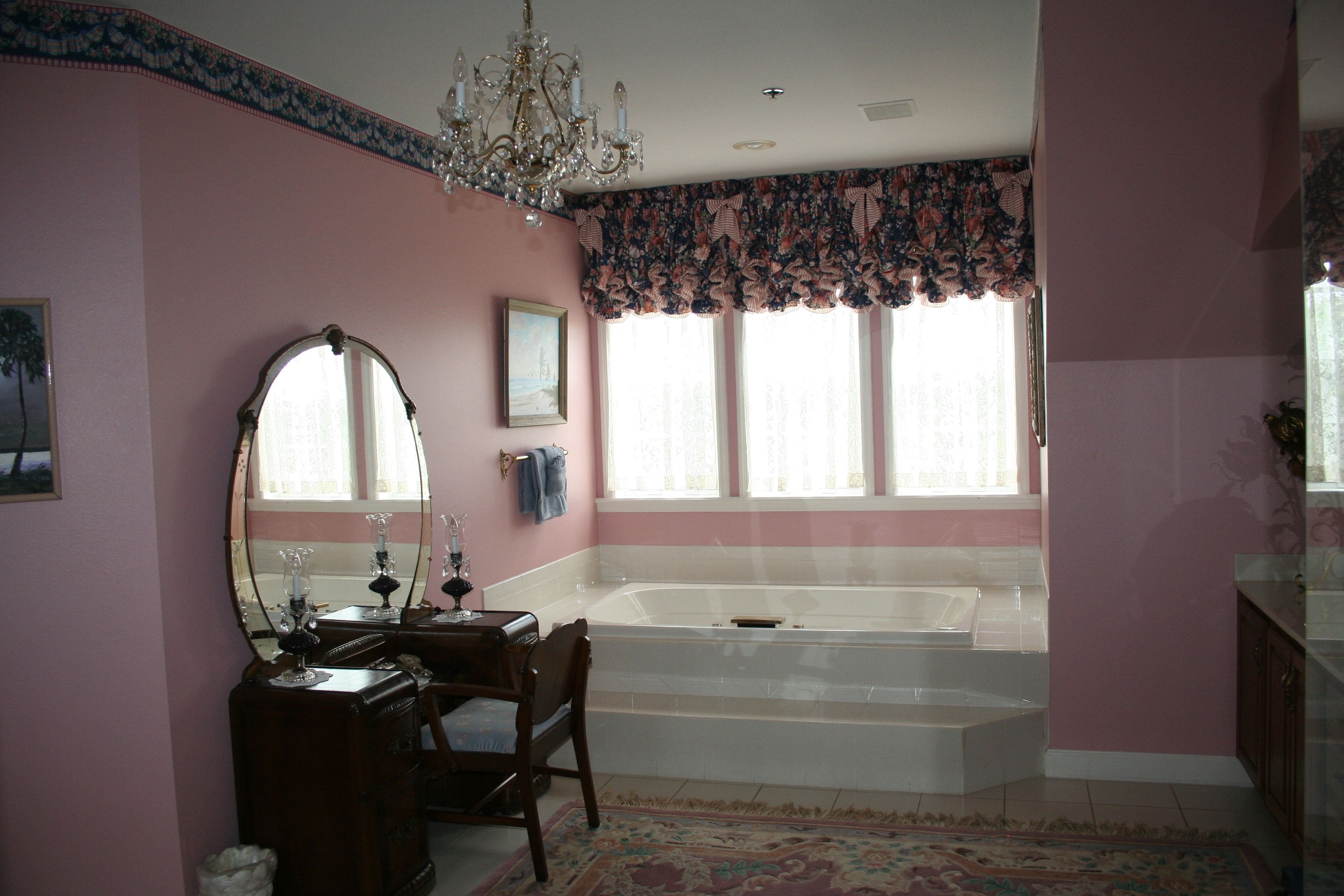 A bathroom with a bathtub, vanity, mirror, chandelier, and floral window valance.