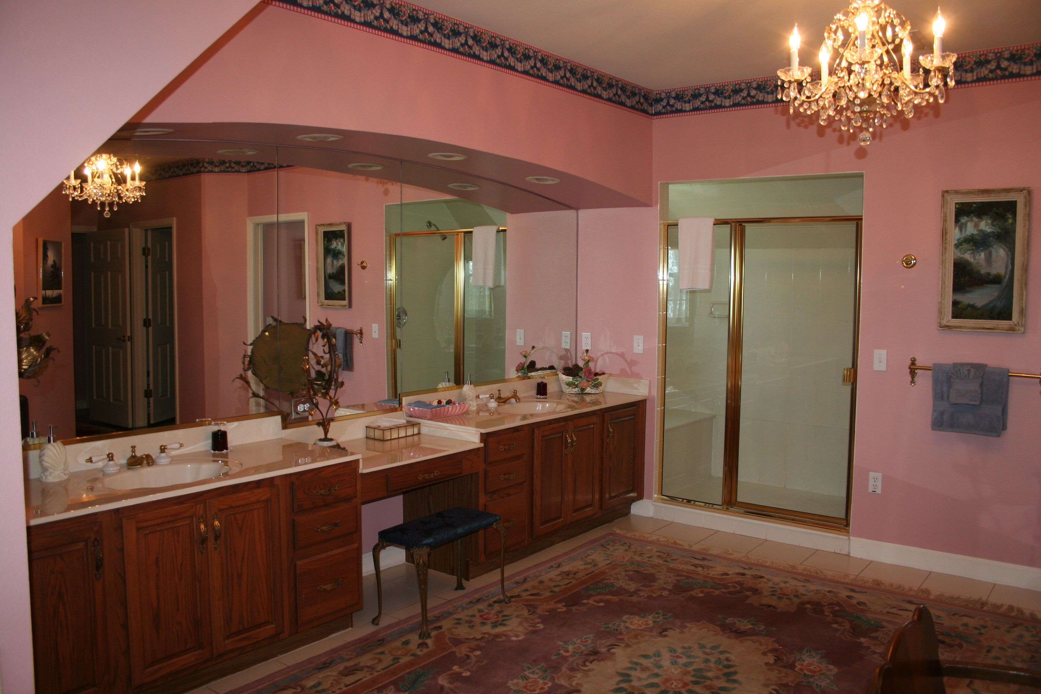 Un bagno con doppio lavabo, doccia con porta in vetro, lampadario e tappeto a motivi.
