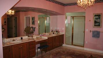 A bathroom with a double vanity, a shower with a glass door, a chandelier, and a patterned rug.