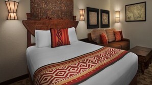 A hotel room with a large bed, two wall-mounted lamps, a patterned headboard, a sofa with cushions, and a framed map on the wall. - Disney's Animal Kingdom Villas - Jambo House (Lake Buena Vista)