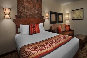 A hotel room with a large bed, two wall-mounted lamps, a patterned headboard, a sofa with cushions, and a framed map on the wall. - Disney's Animal Kingdom Villas - Jambo House (Lake Buena Vista)