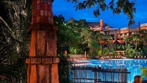 A resort with a swimming pool, a stone tower, and lush greenery.