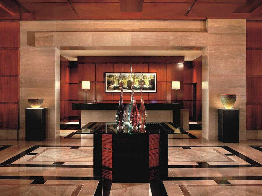 Un hall d’entrée avec un comptoir de réception, une grande œuvre d’art encadrée au-dessus, et deux vases décoratifs posés sur des supports.
