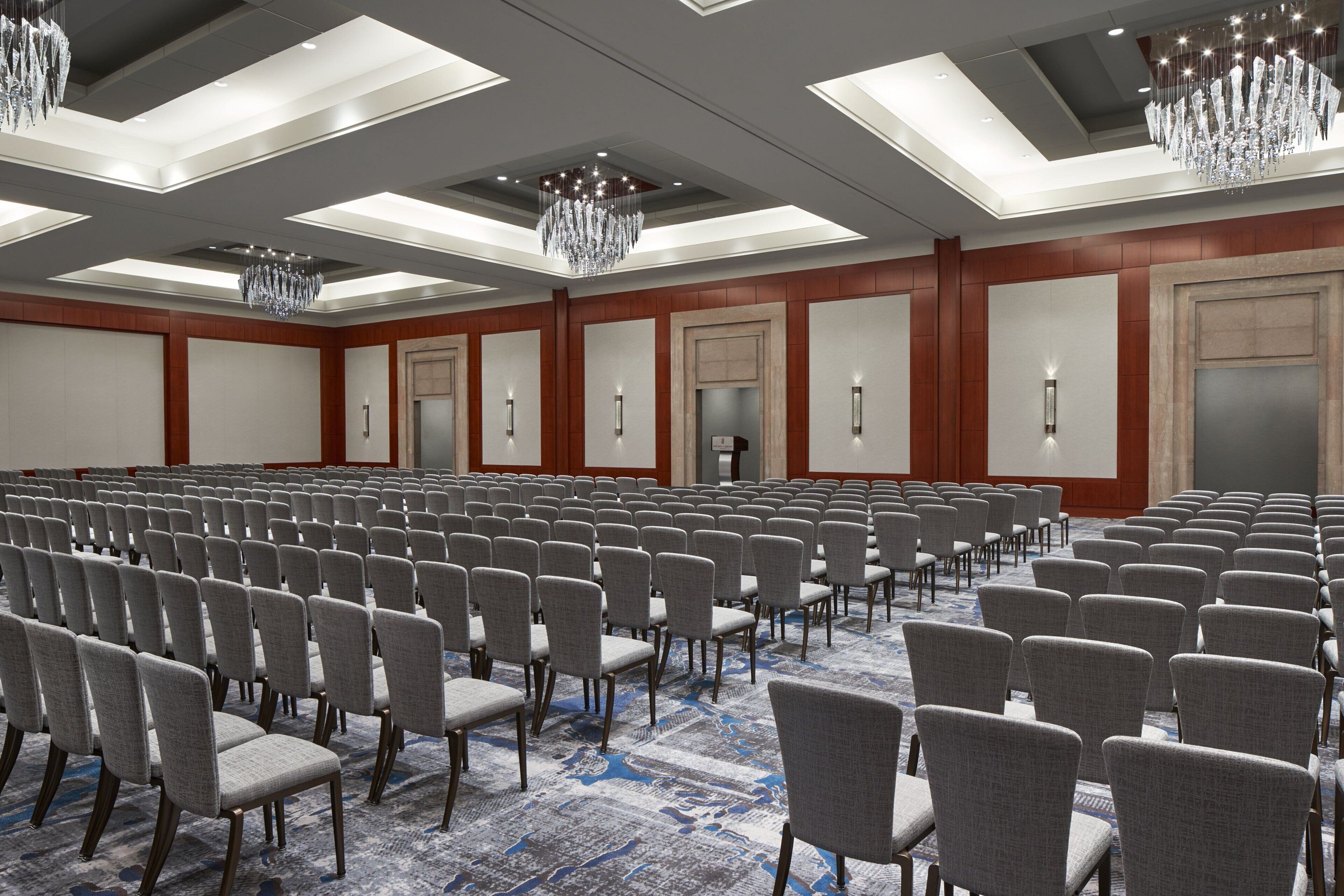 A large conference room with rows of chairs, a patterned carpet, and chandeliers.