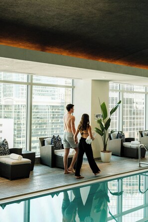 A modern indoor pool area with a glass barrier, lounge chairs, and a large potted plant. - The Ritz-Carlton, Charlotte (Charlotte)