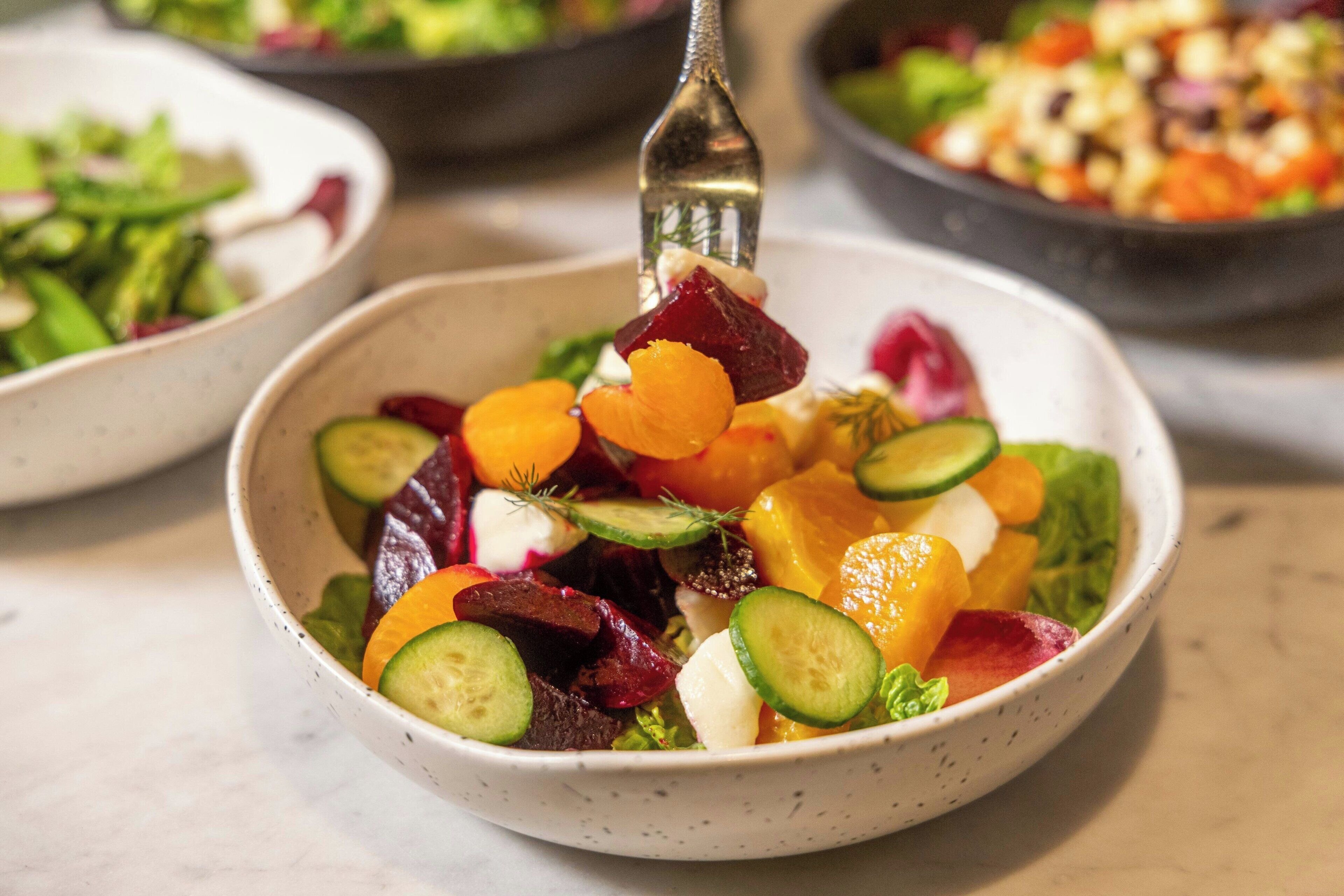 A bowl of salad with various vegetables and a fork.