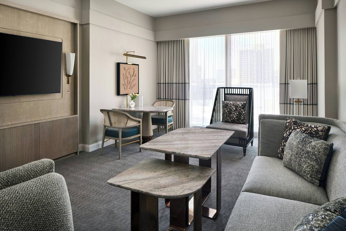 A modern hotel room with a large flat-screen TV, a dining table, a sofa, and a chair.