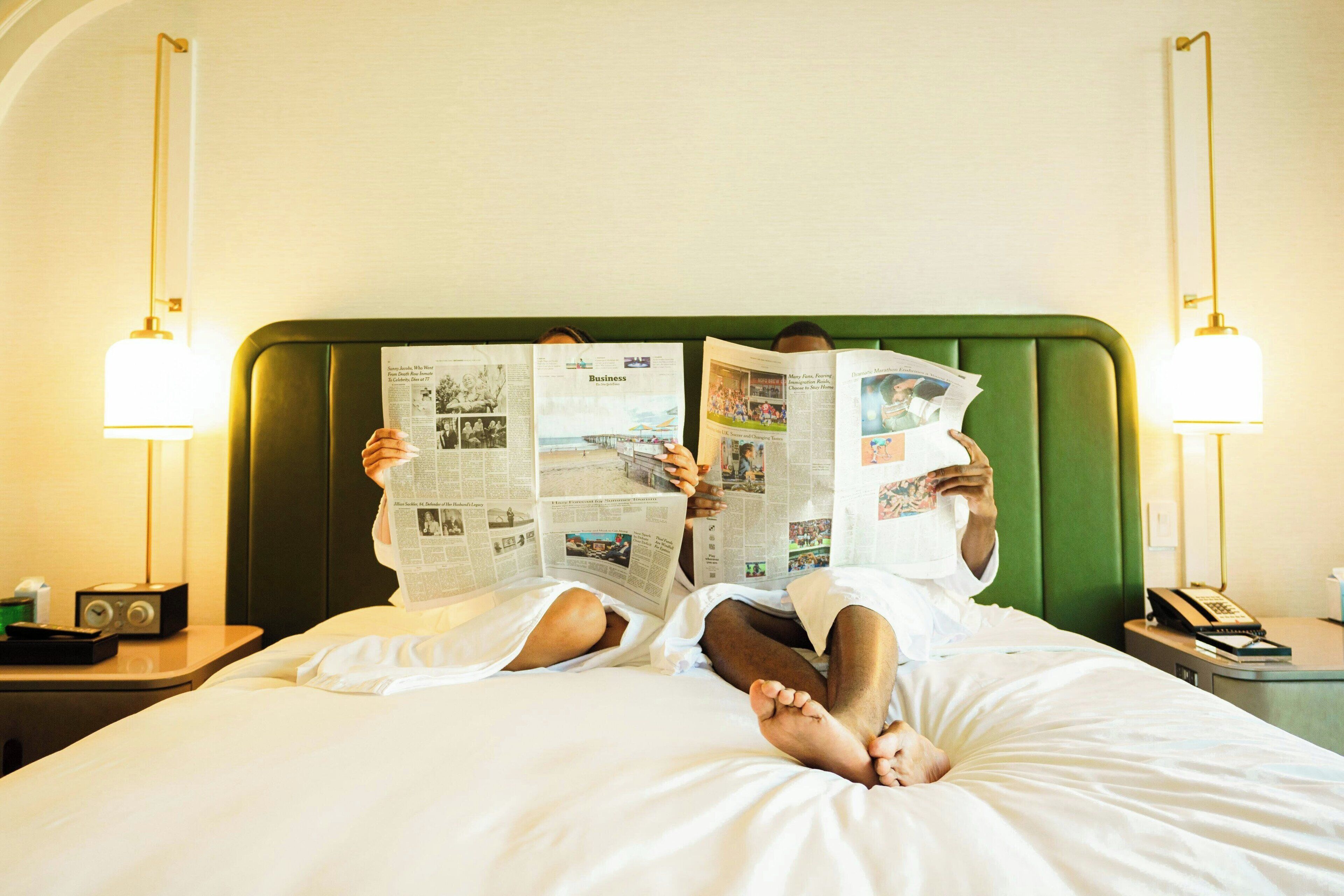Twee personen liggen in bed en lezen kranten.