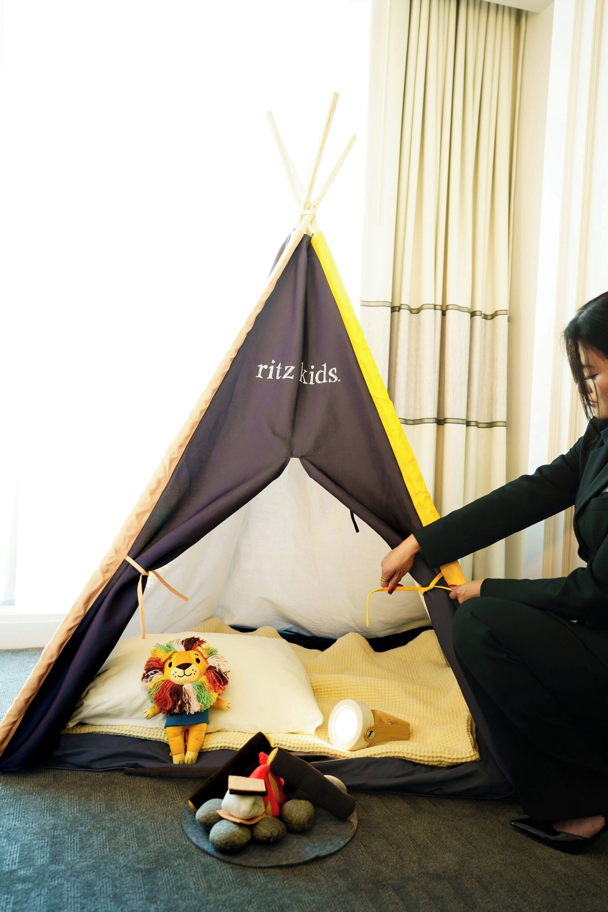 A tent set up in a room with a plush toy lion, a lamp, and a small toy train.