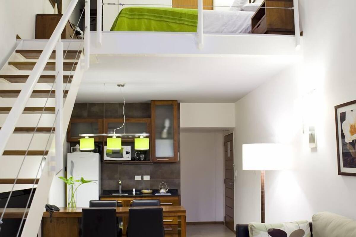 A compact living space with a loft bed, kitchenette, dining area, and a sofa.