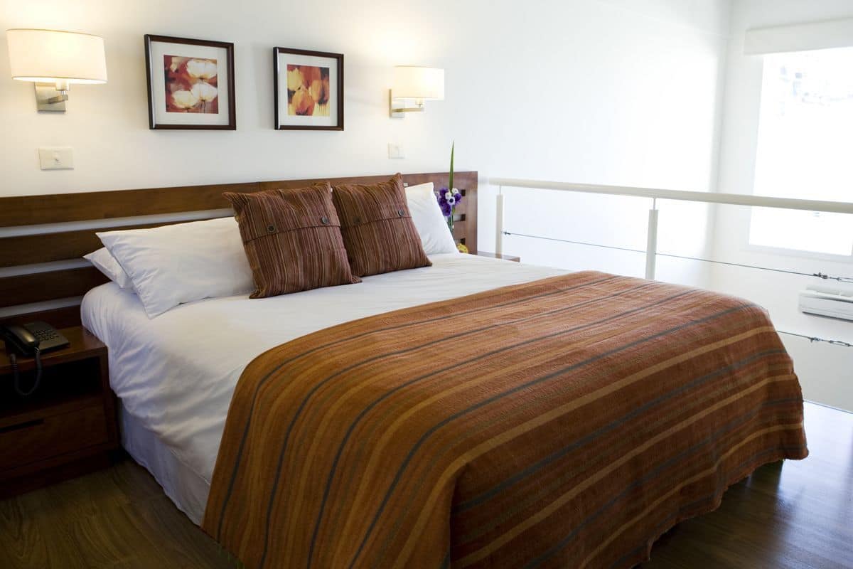A hotel room with a large bed, two wall-mounted lamps, and framed floral artwork.