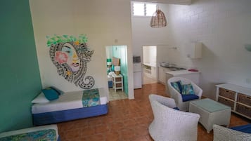 A room with a bed, a sofa, wicker furniture, a kitchen area, and a mural on the wall.