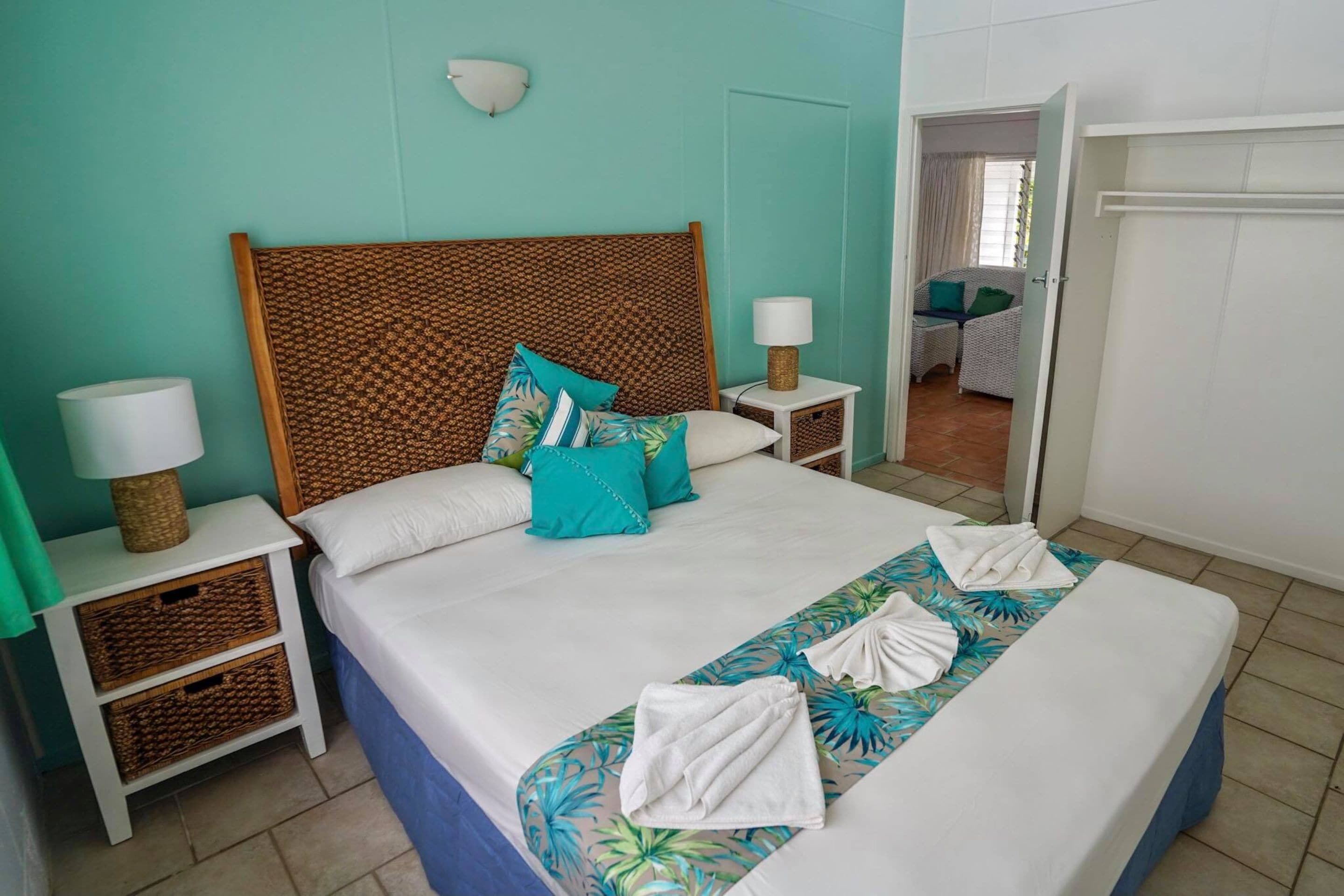 A neatly made bed with a patterned headboard, two bedside tables with lamps, and a view of a balcony through an open door.