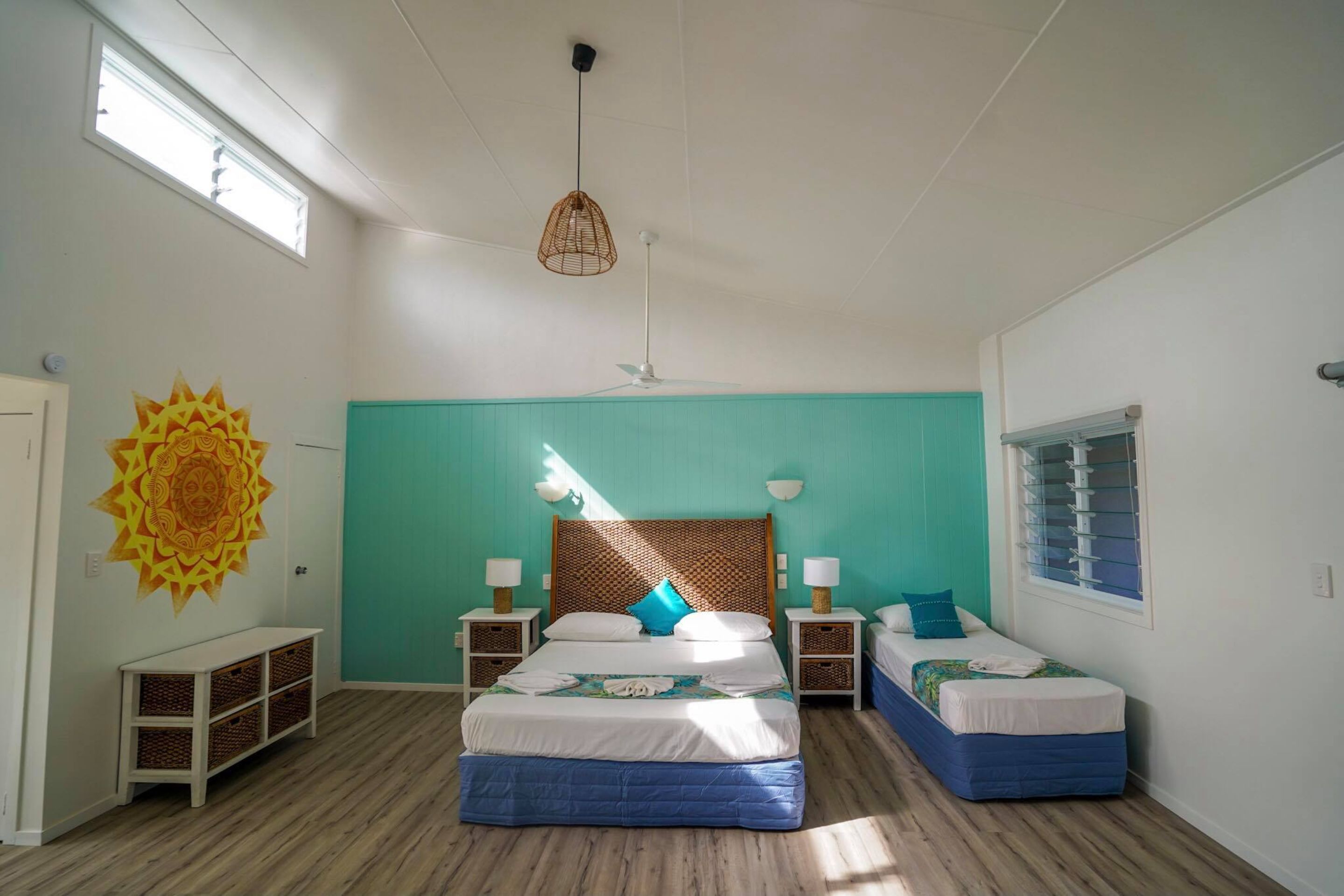 Ein Schlafzimmer mit zwei Betten, einem Deckenventilator, einem Fenster und einer Wanddekoration.