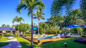 Ein Poolbereich mit Liegestühlen, einem Pool, Palmen und einem Haus im Hintergrund.