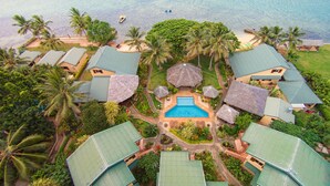 An aerial view of a resort with multiple bungalow-style buildings, a central swimming pool, and a beach area. - Poppys On The Lagoon (Port Vila)