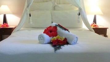 Una cama bien hecha con una colcha blanca, una toalla enrollada y un arreglo floral.