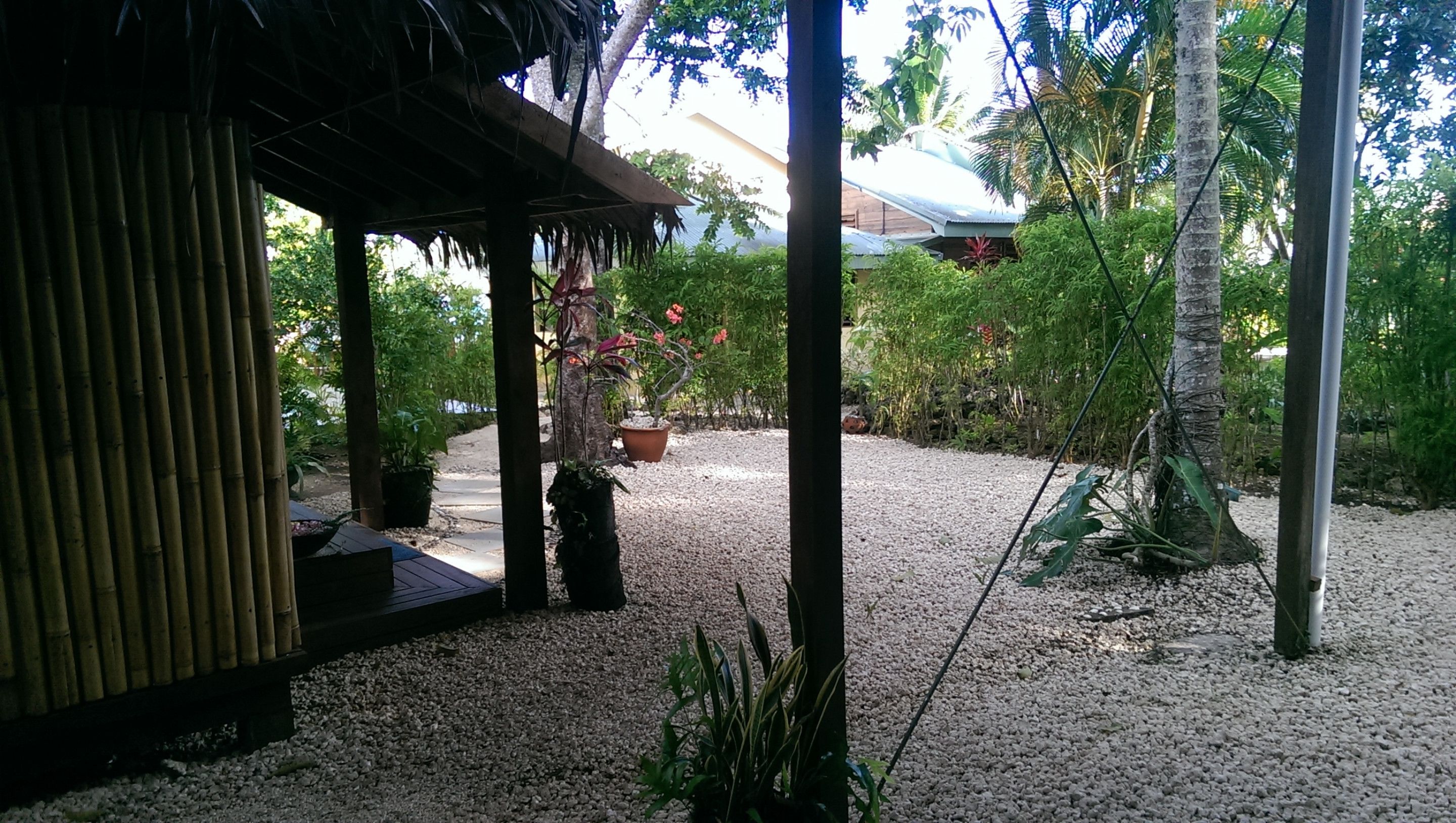 Un espacio al aire libre cubierto con un camino de grava, columnas de bambú y plantas en macetas.