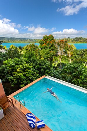 A swimming pool with a wooden deck, lounge chairs, and a person swimming. - Poppys On The Lagoon (Port Vila)