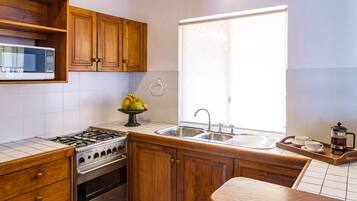 Una cocina con armarios de madera, una estufa de acero inoxidable, un microondas, un fregadero y una ventana con cortina.