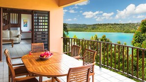 A wooden dining table with chairs and a bowl of fruit on a balcony with a view of a turquoise sea and green hills. - Poppys On The Lagoon (Port Vila)
