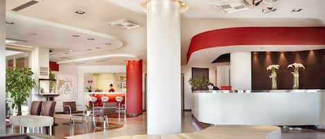 Um hall de hotel moderno com balcão de recepção, área de estar e uma coluna grande.