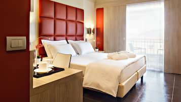 A modern hotel room with a large bed, a wooden desk, and a view of the outside through large windows.