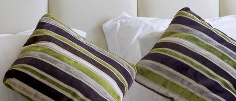 Una cama bien hecha con almohadillas a rayas y una bandeja con tazas y platillos blancos.