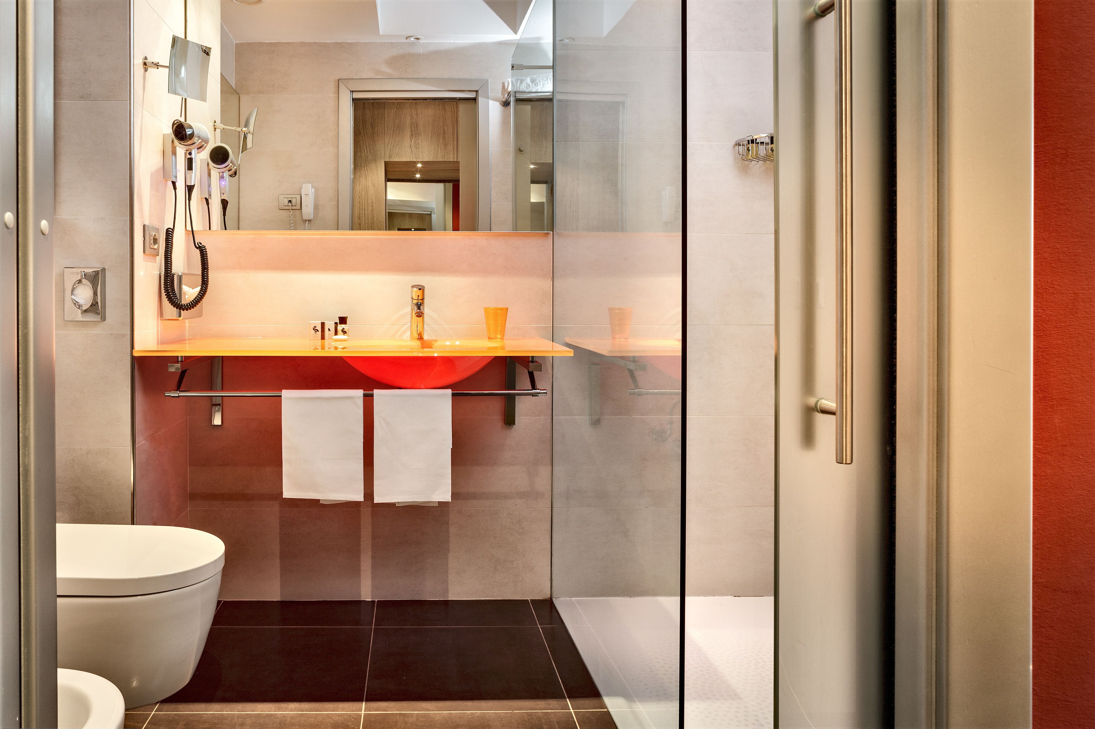 A modern bathroom with a glass shower enclosure, a white toilet, and a vanity with a red sink.