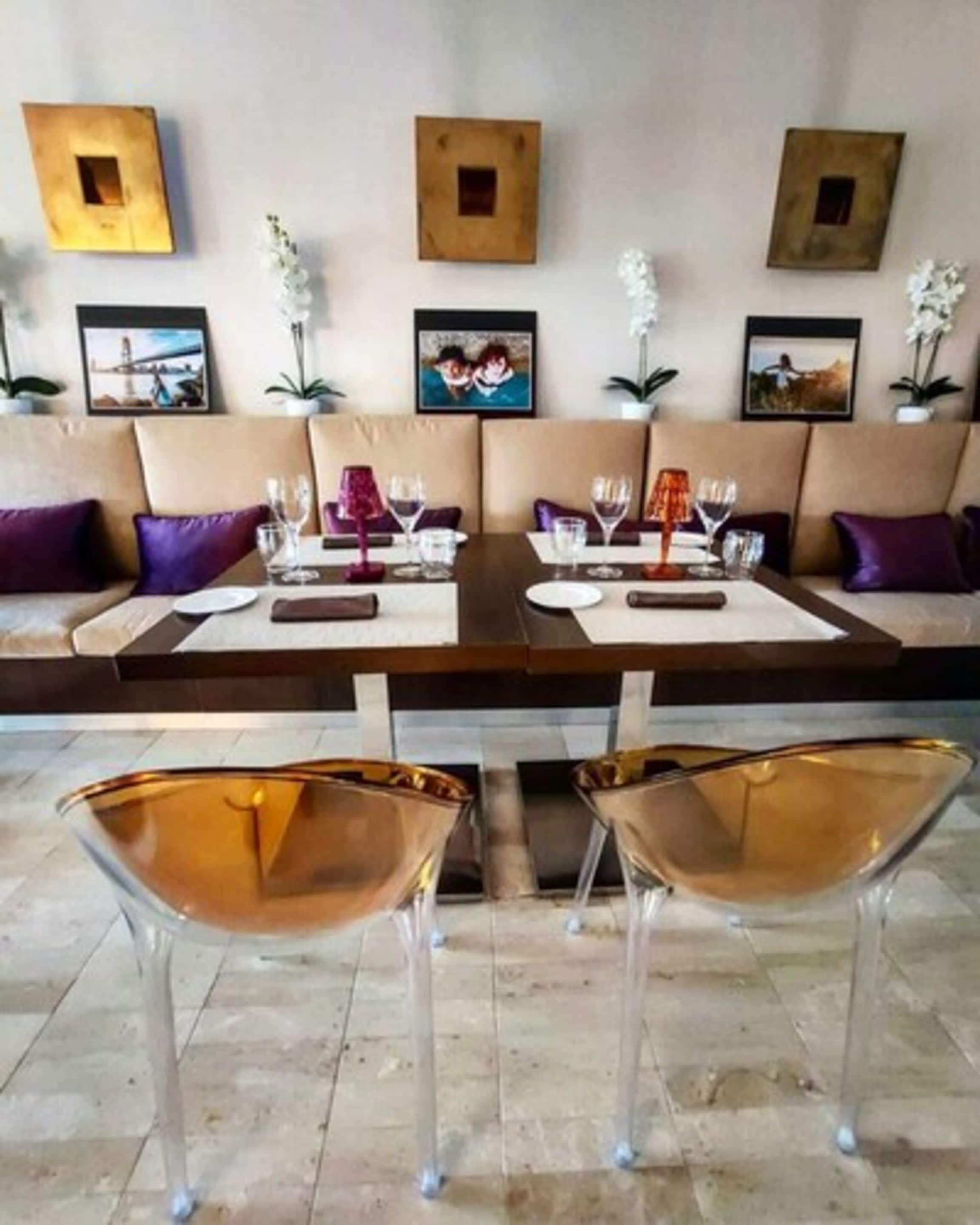 A dining area with a long table, two chairs, and a sofa with cushions.