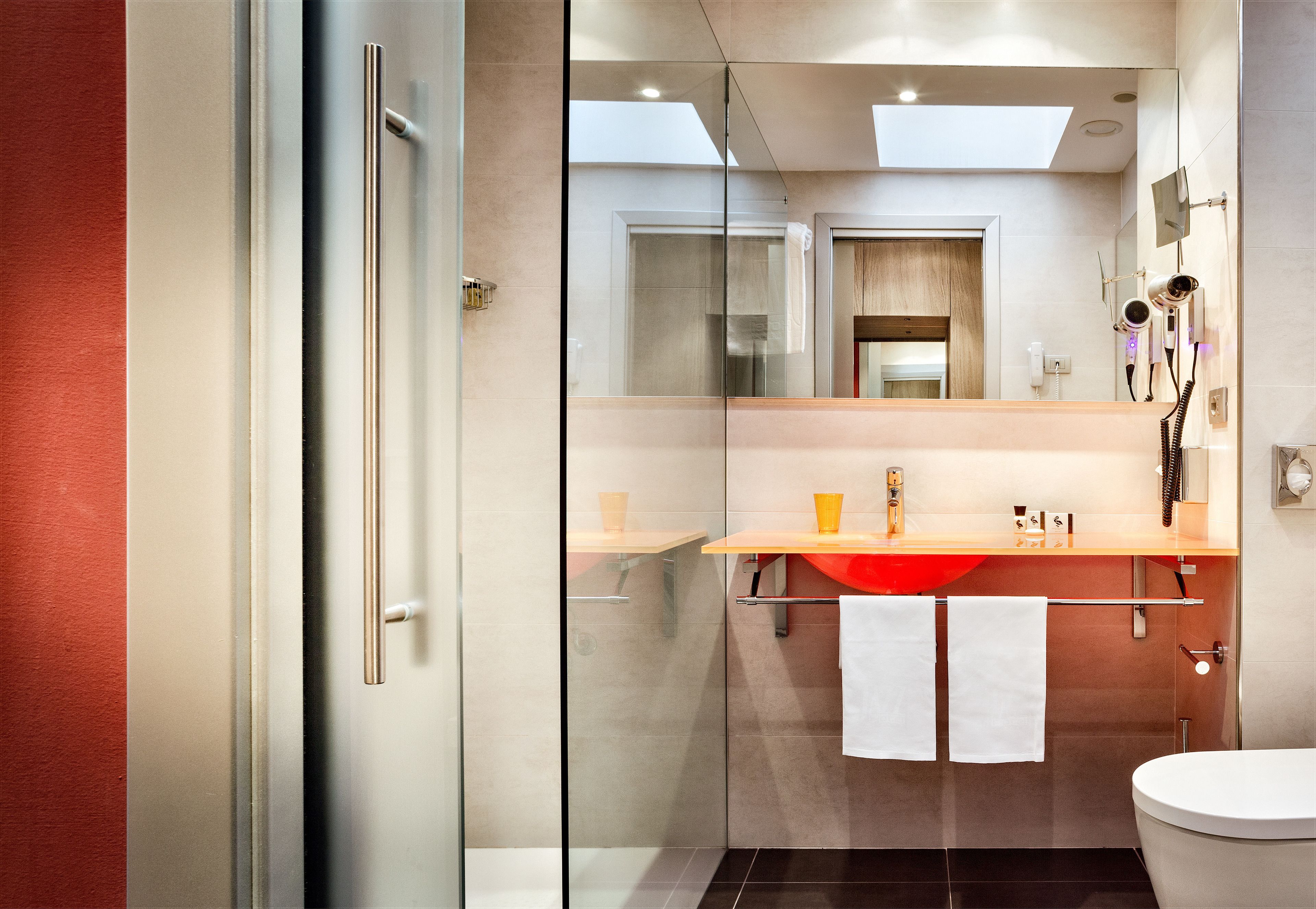 A modern bathroom with a glass shower enclosure, a wooden vanity with a red sink, and a white toilet.