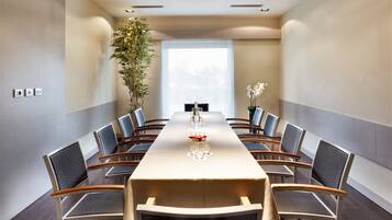 Un salón de conferencias con una larga mesa, sillas, una planta en maceta y un ventanal.