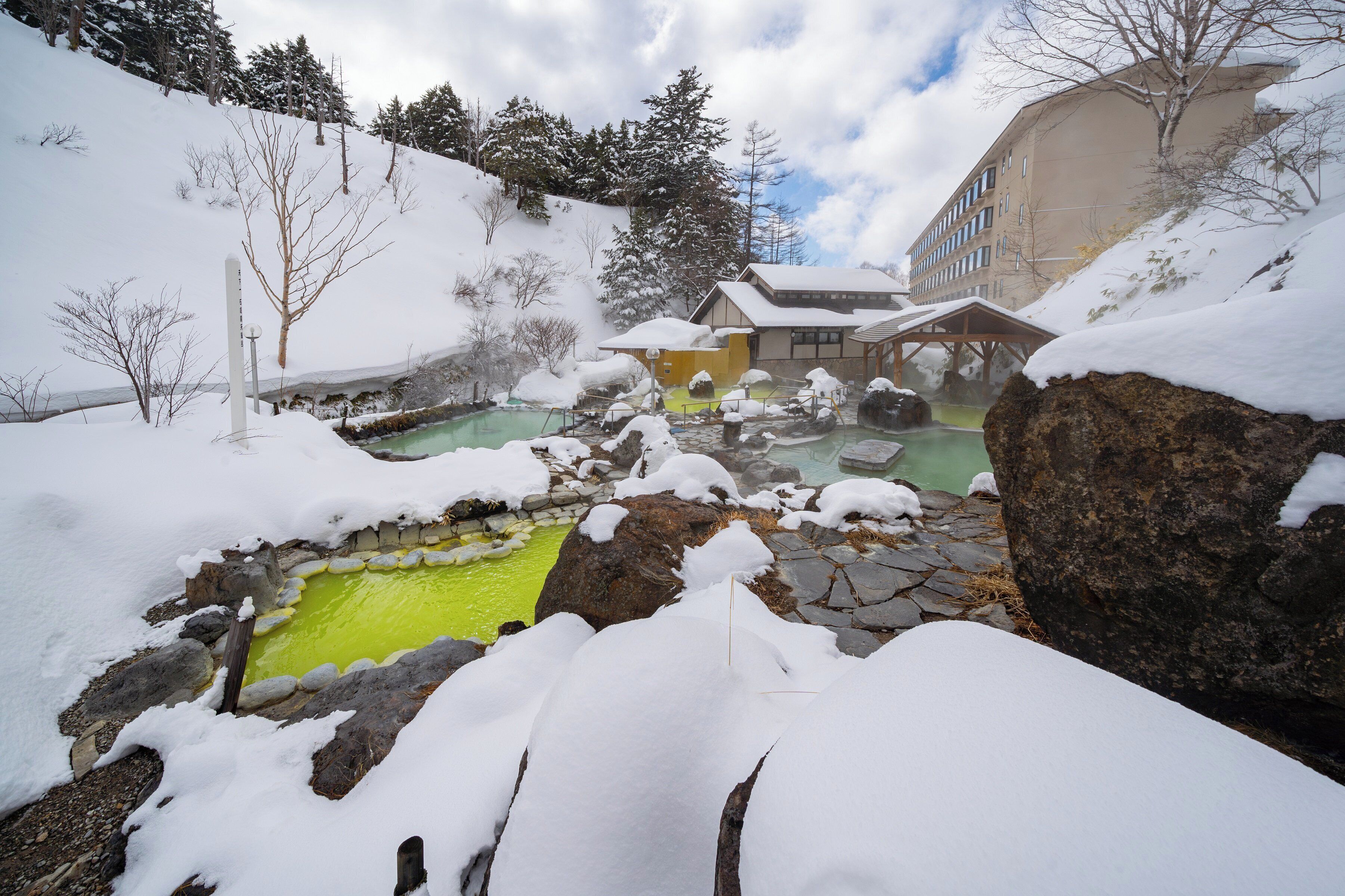 A snow-covered outdoor area with a stone pool and a building with a snow-covered roof.