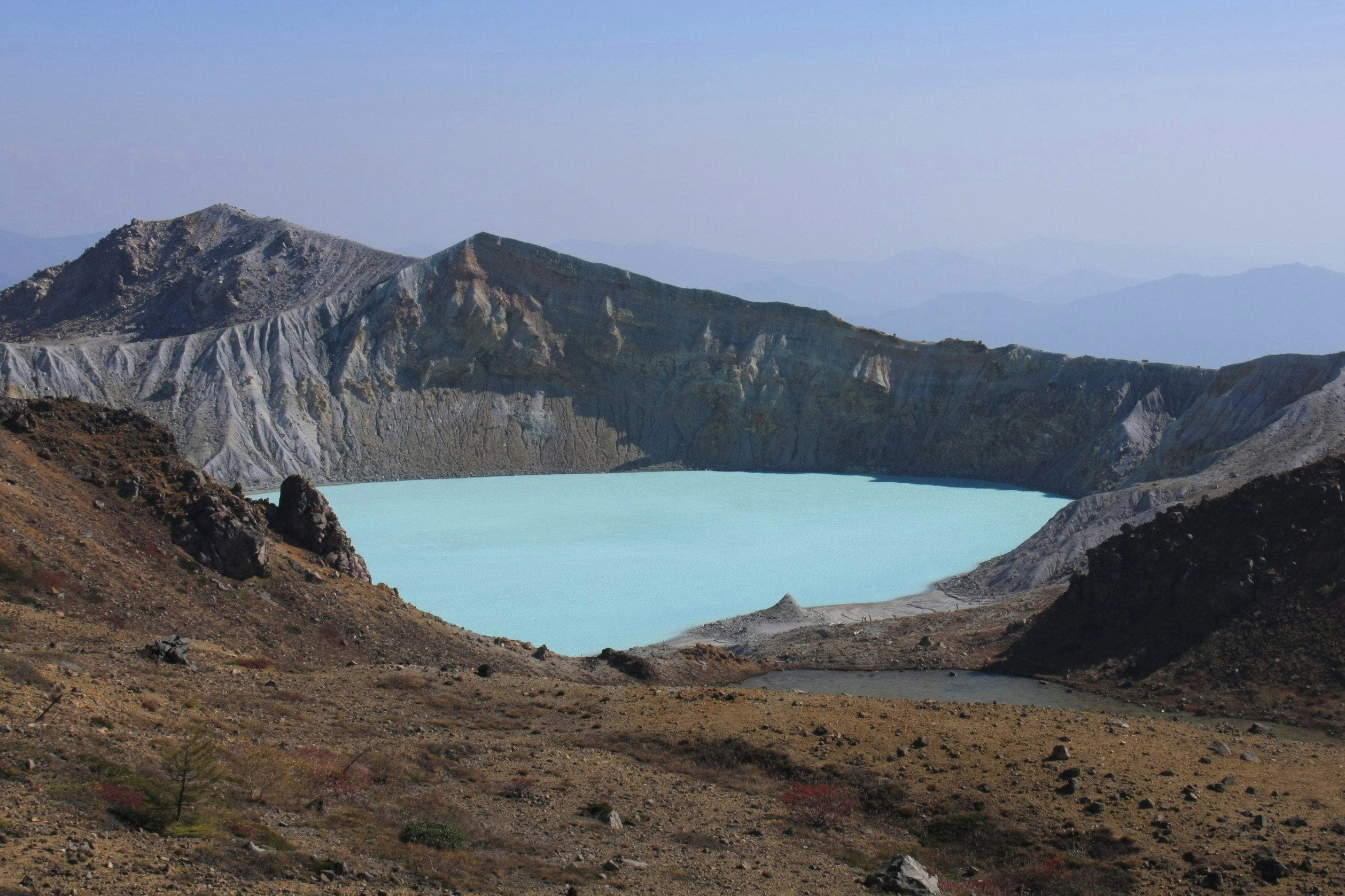 A natural landscape with a large, clear blue lake surrounded by rugged terrain and mountains.