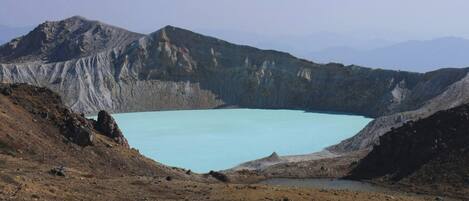 Un paisaje natural con un lago azul grande y transparente rodeado de terreno escarpado y montañas.