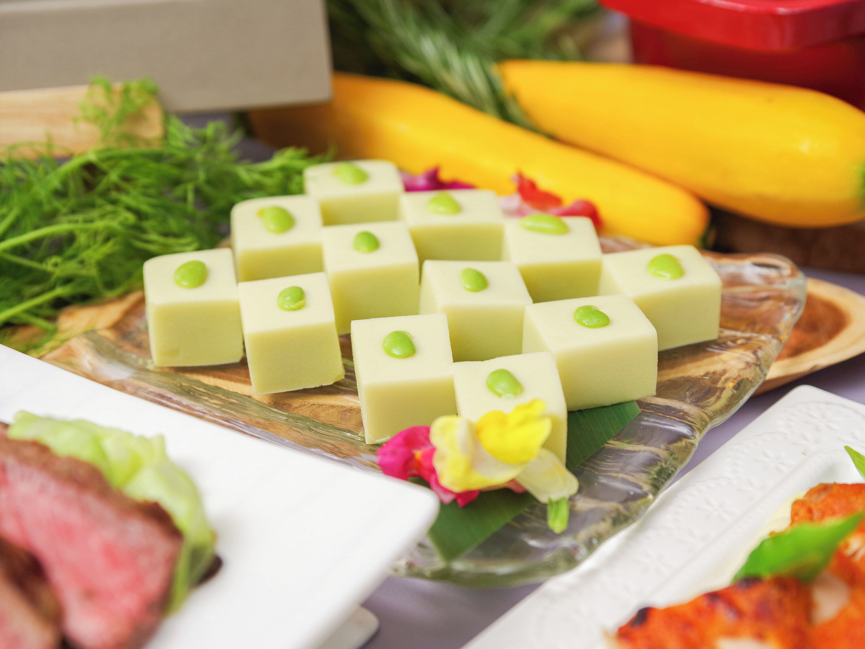A table with various food items including a dish with green toppings, a plate with meat, and some vegetables.