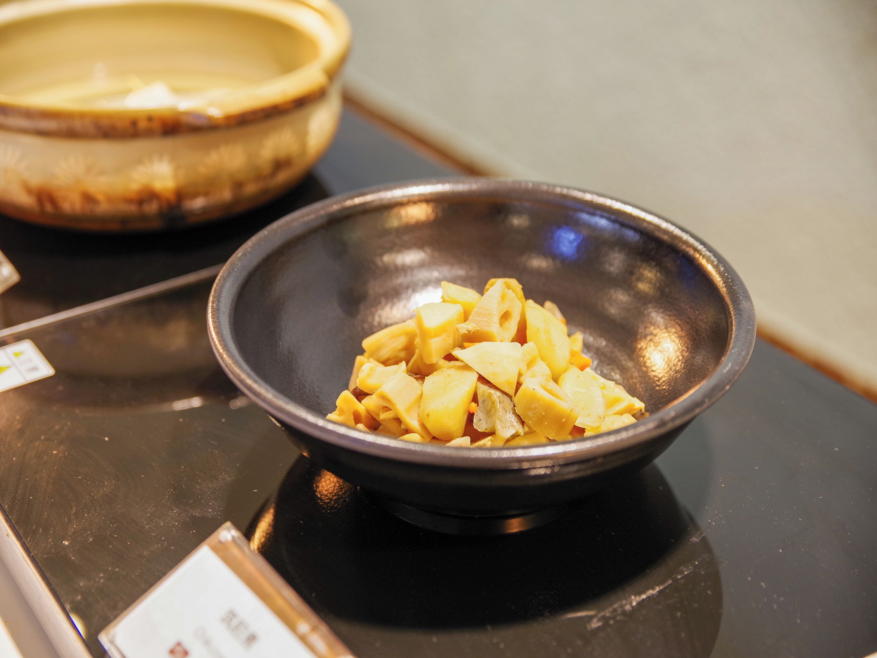 A black bowl containing diced yellow fruit on a reflective surface.