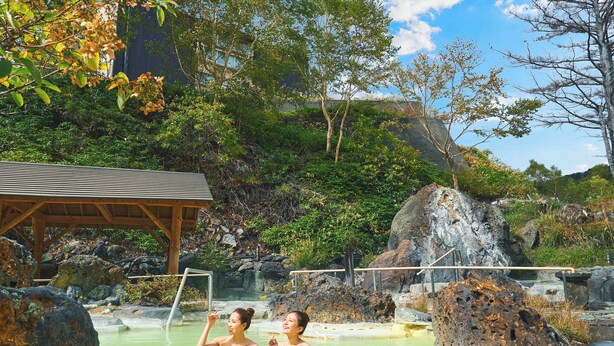 A natural hot spring area with two people in the water, surrounded by rocks and greenery. - Manza Kogen Hotel (Tsumagoi)
