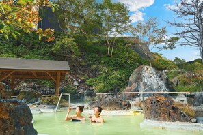 Une zone de sources chaudes naturelles où l’on voit deux personnes dans l’eau, entourées de rochers et de végétation.