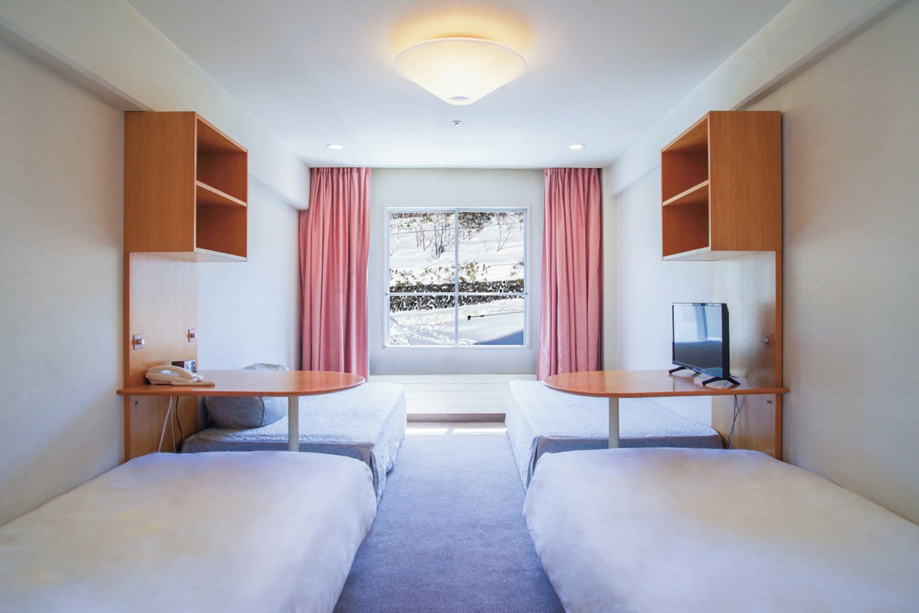 Habitación de hotel con dos camas, un escritorio, un televisor y una ventana con cortinas.