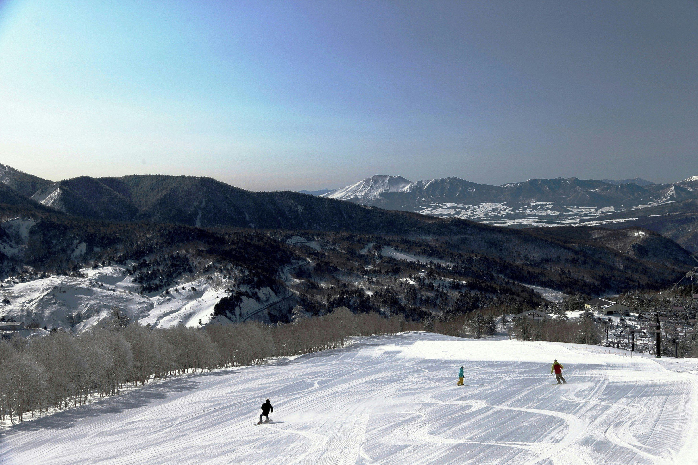 A ski slope with skiers, a mountain backdrop, and a clear sky.
