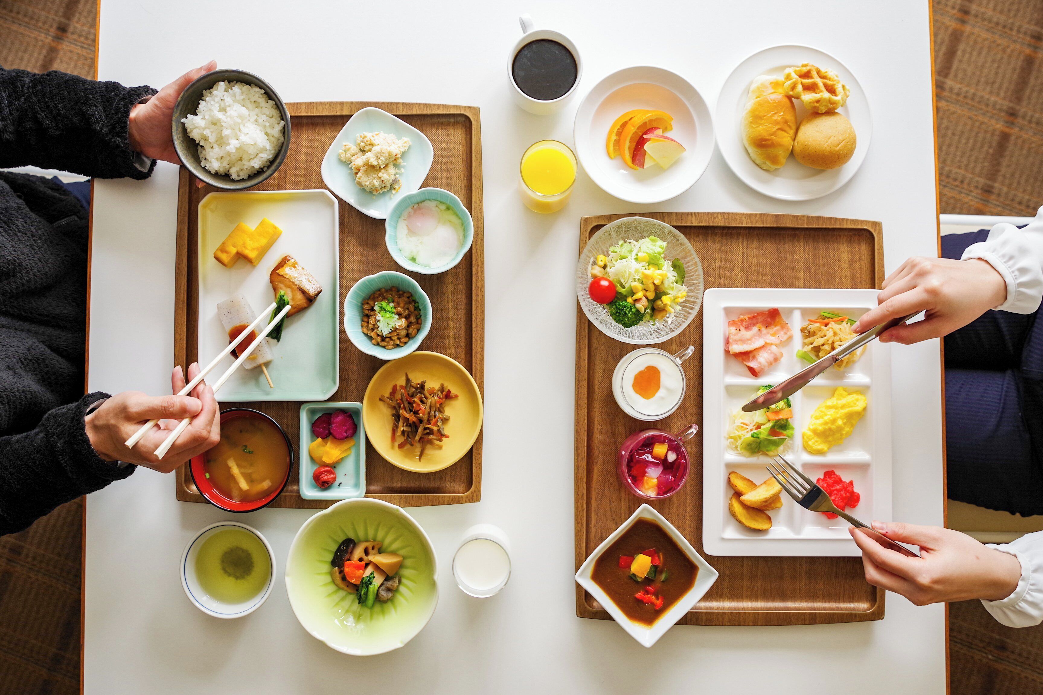 A dining table with various dishes, including rice, soup, and vegetables, and two people using chopsticks and forks.