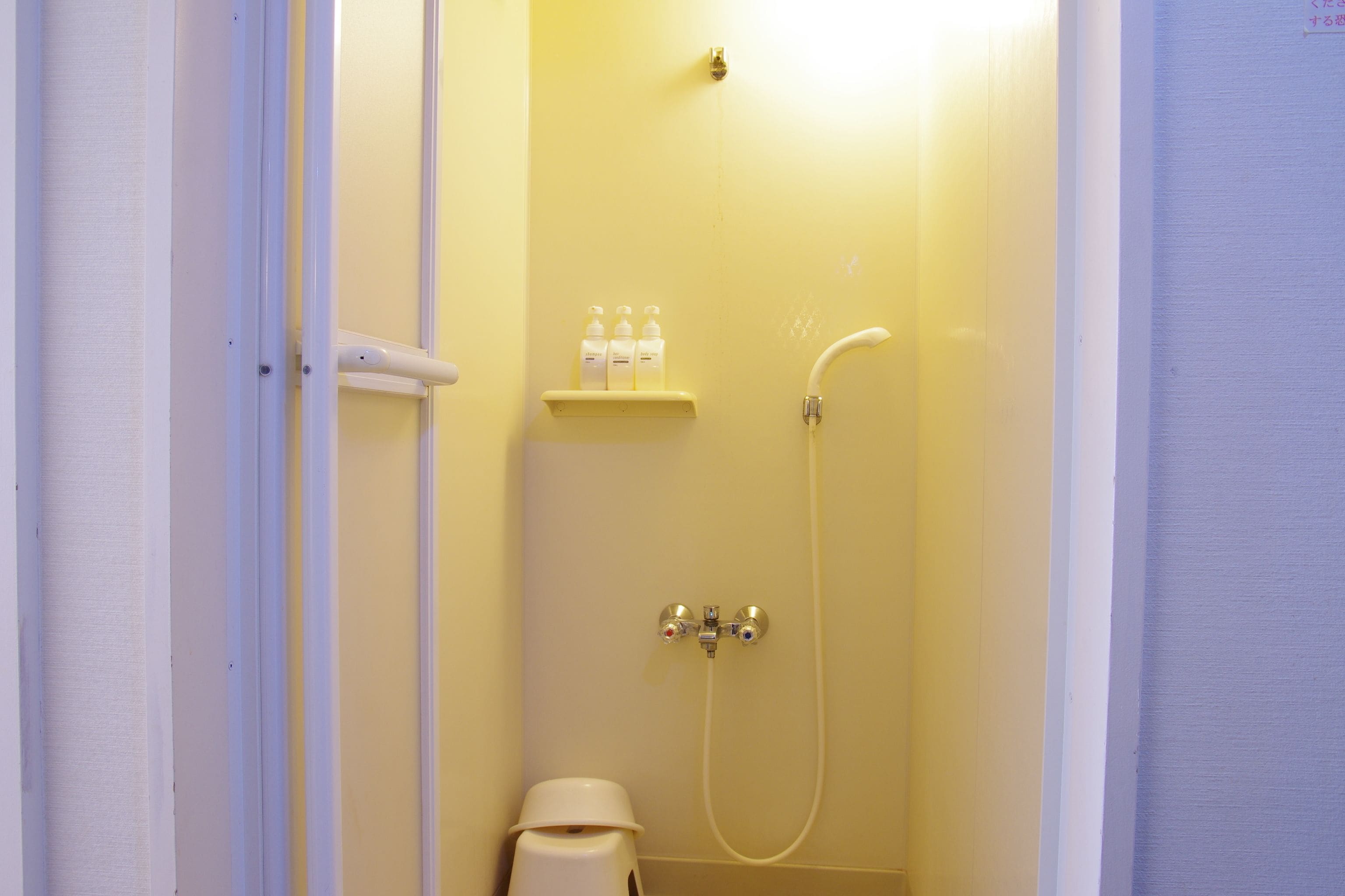 A small, enclosed shower area with a shelf holding bottles, a handheld showerhead, and a toilet.