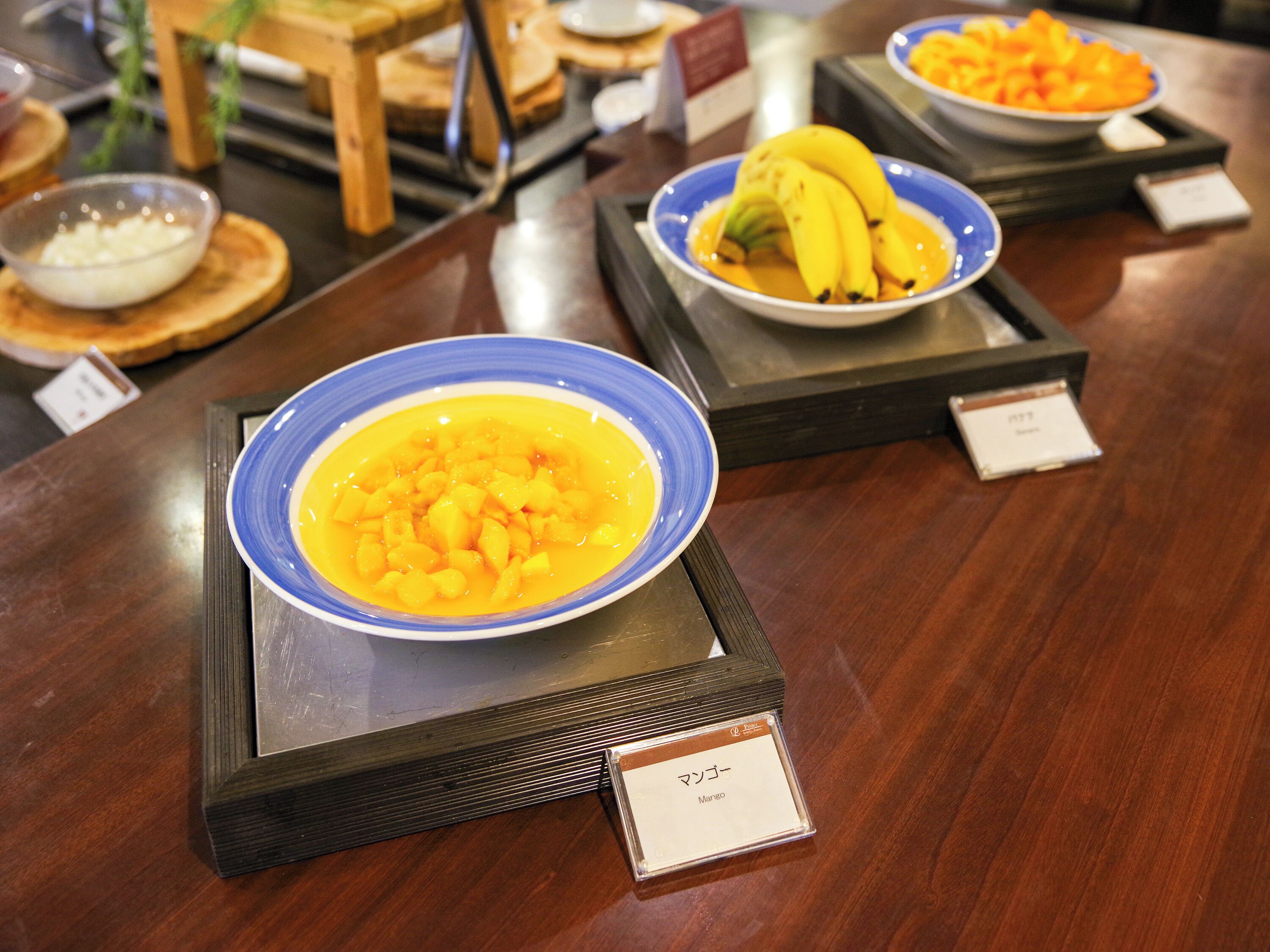 En buffet med forskellige retter, heriblandt en skål med mangosalat, en skål med mangostykker og en skål med mango i skiver.