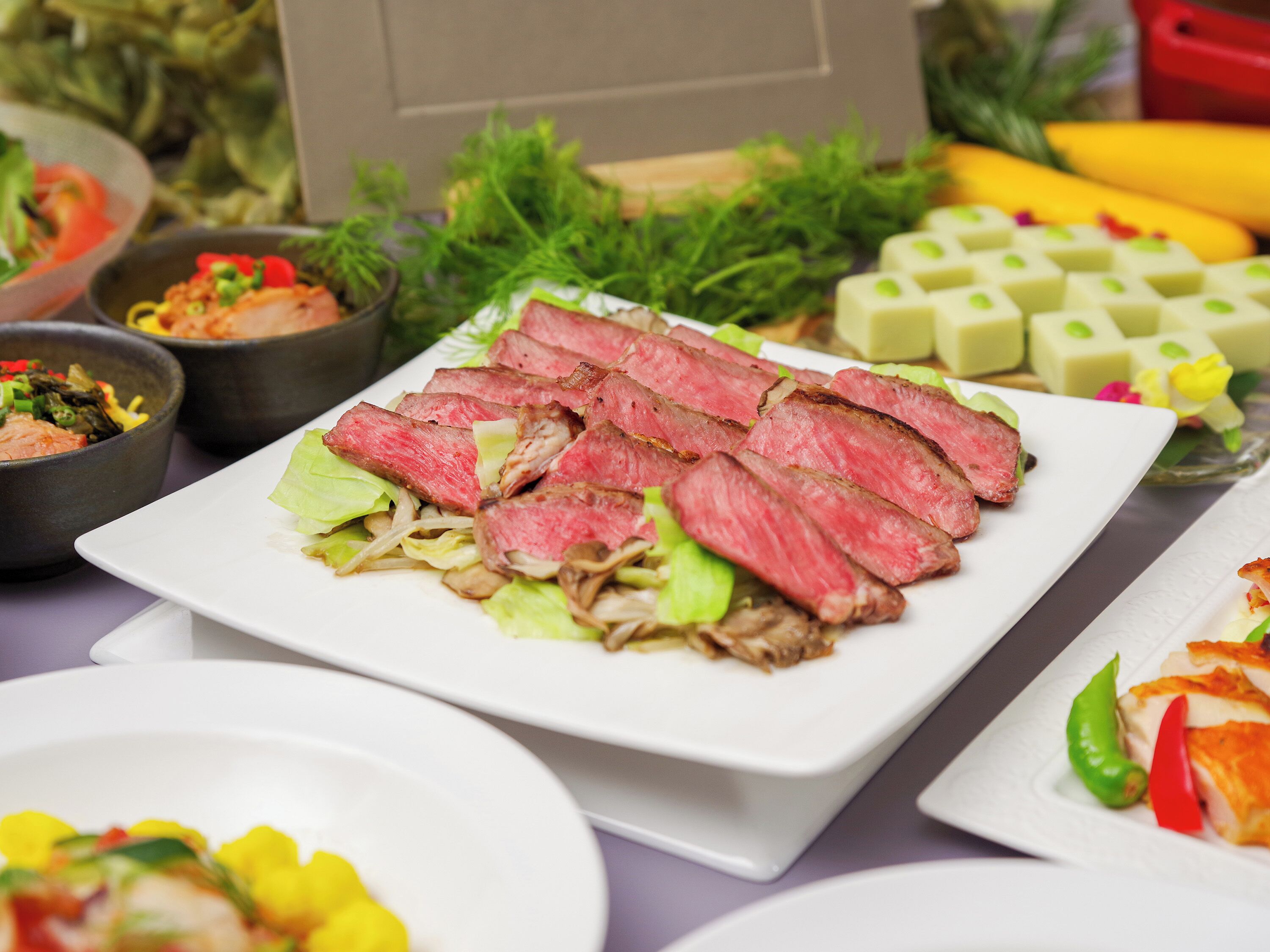 Ein Tisch mit verschiedenen Speisen, darunter geschnittenes Fleisch, Gemüse und Beilagen.