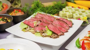 Ein Tisch mit verschiedenen Speisen, darunter geschnittenes Fleisch, Gemüse und Beilagen.