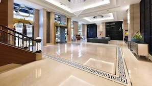 En rummelig lobby med en imponerende lysekrone, en receptionsdisk og en trappe.